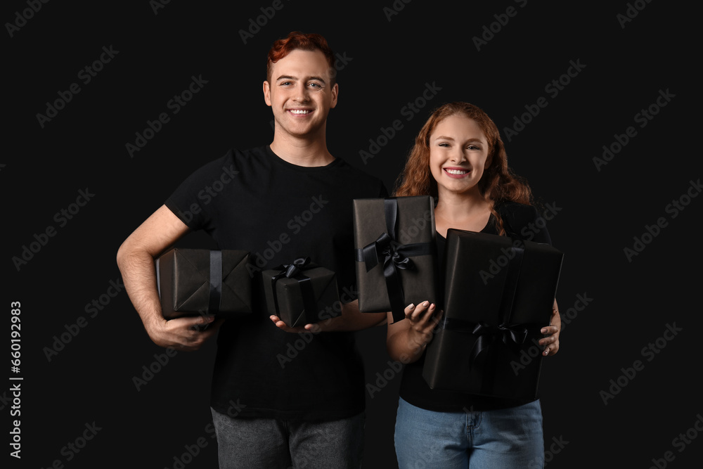 Beautiful young couple with gift boxes on dark background. Black Friday sale