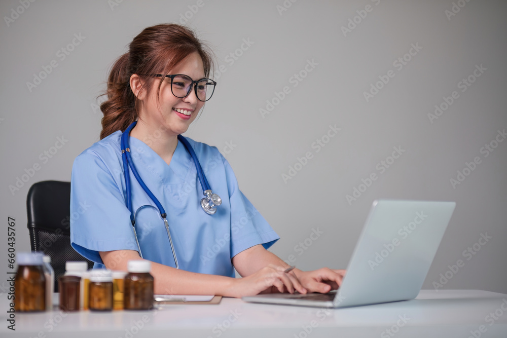 Young beautiful doctor holding pill bottle explaining details about medicine via laptop online at clinic