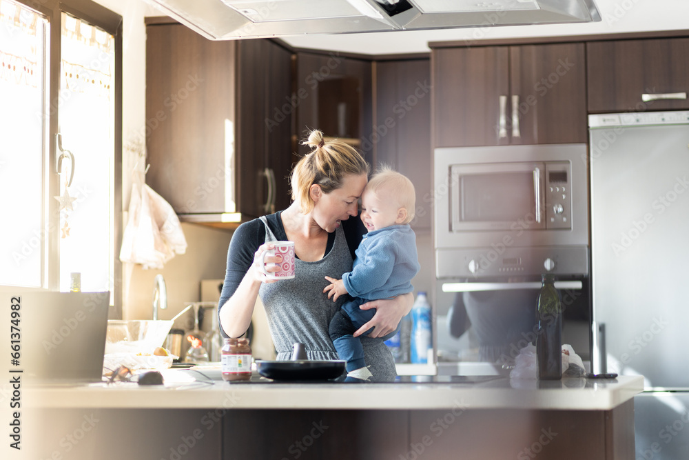 Happy mother and little infant baby boy together making pancakes for breakfast in domestic kitchen. Family, lifestyle, domestic life, food, healthy eating and people concept