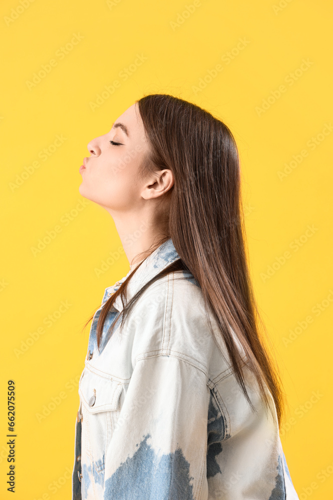 Young woman blowing kiss on yellow background