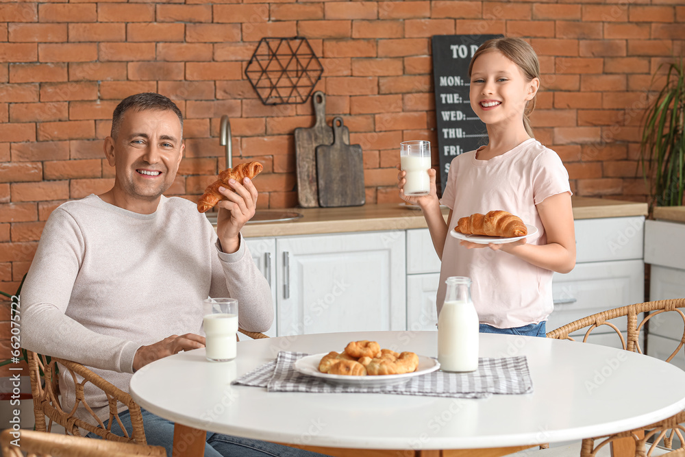 Little girl with her father sitting at table and drinking milk in kitchen