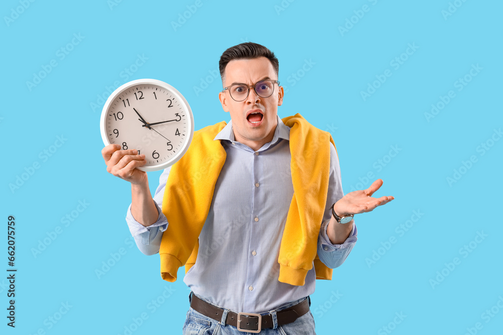 Stressed businessman with clock on blue background. Deadline concept