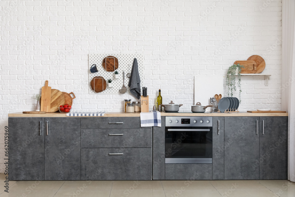 Grey counters with cutting boards, utensils, oven and electric stove in modern kitchen