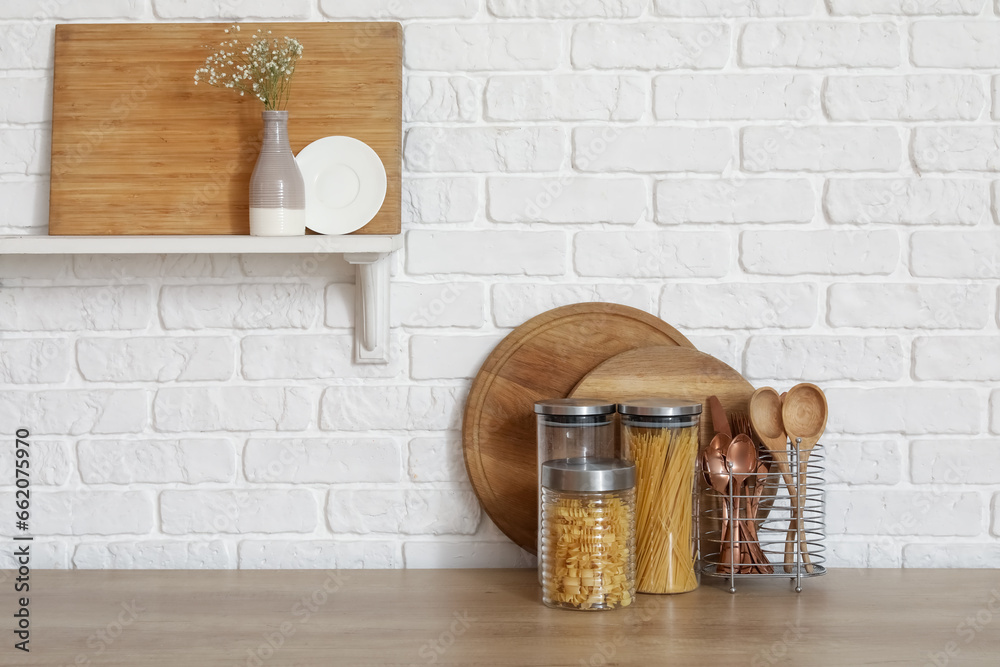 Wooden countertop with cutting boards and utensils near white brick wall