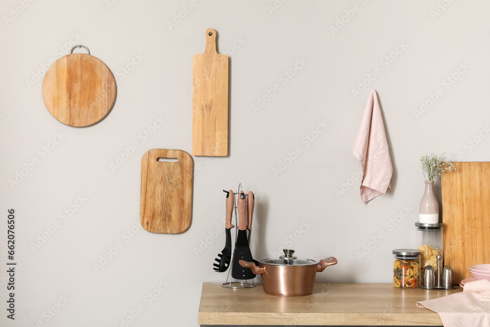 Wooden kitchen counter with cooking pot, utensils and cutting boards hanging on white wall