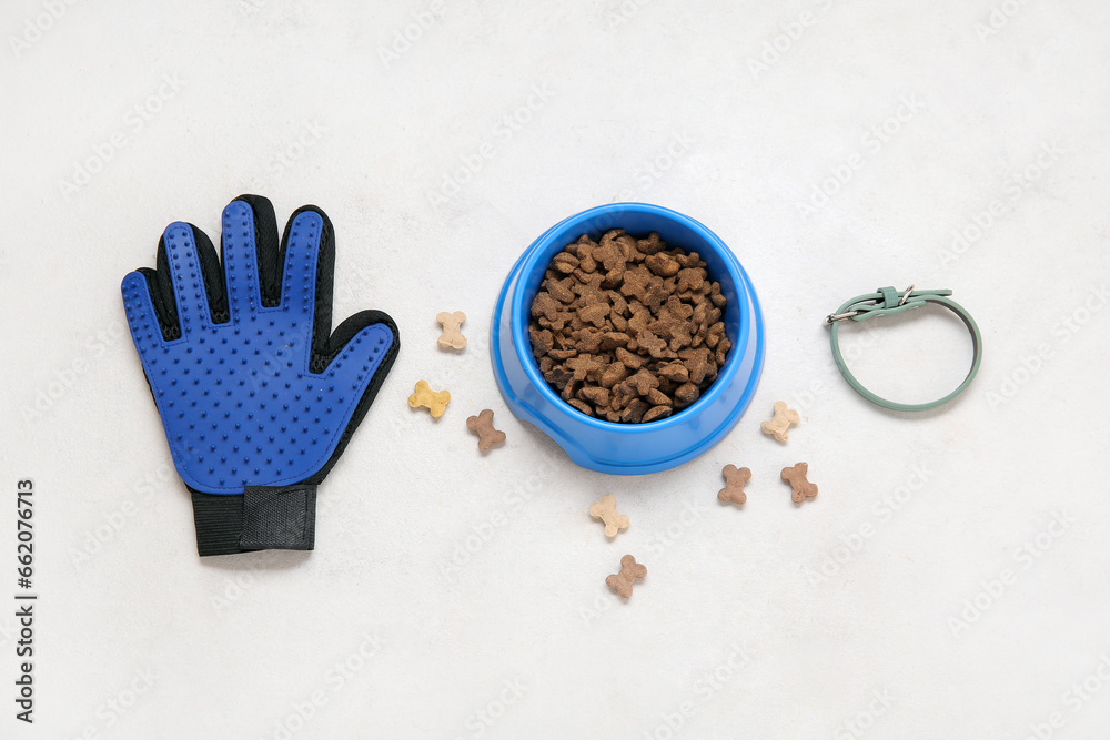 Pet collar, bowl of dry food and grooming glove on light background