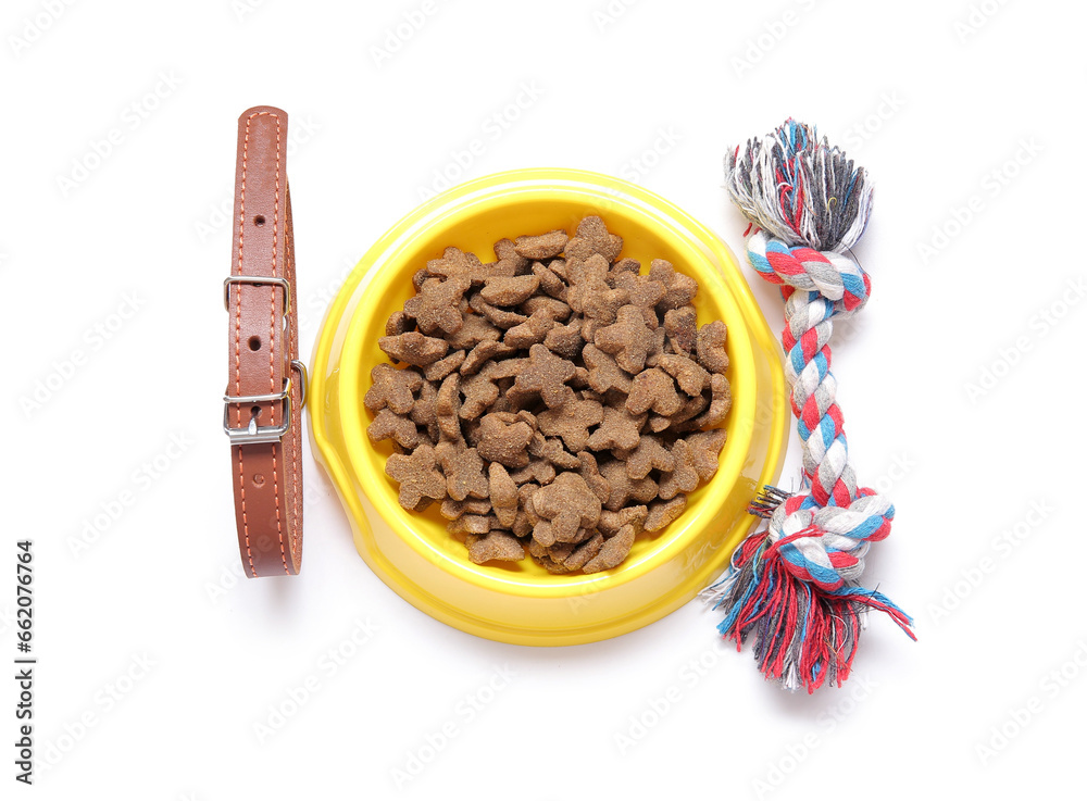 Bowl of dry pet food, collar and cotton toy on white background