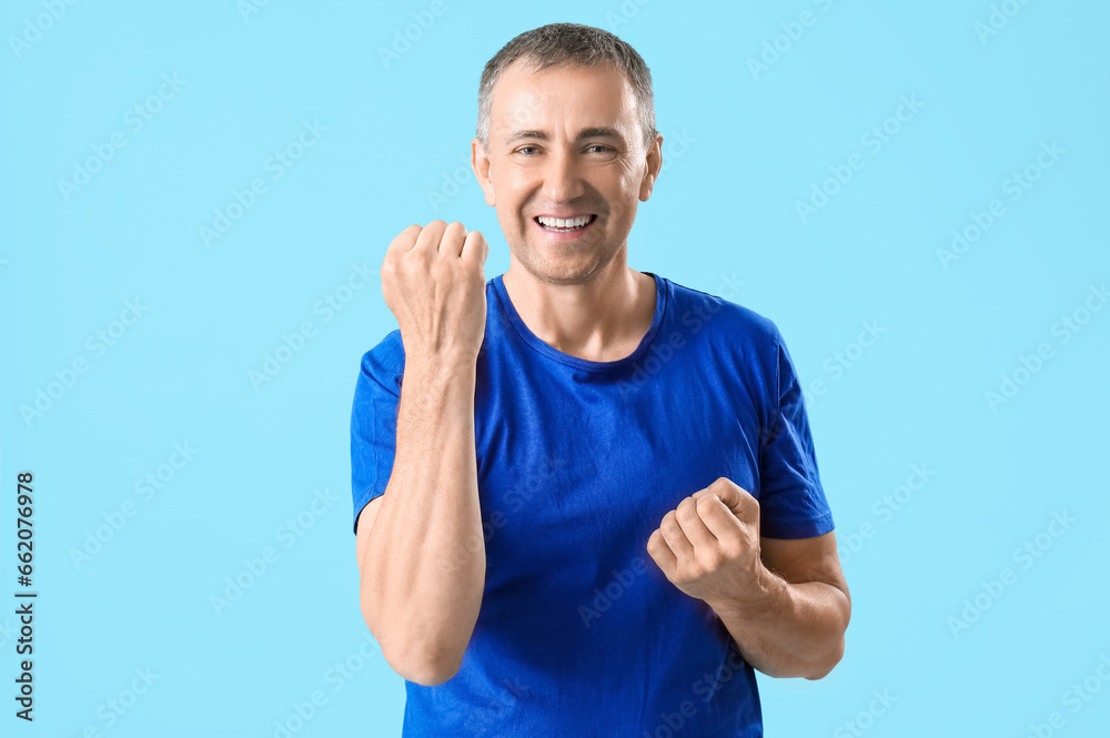 Portrait of happy mature man celebrating success on blue background