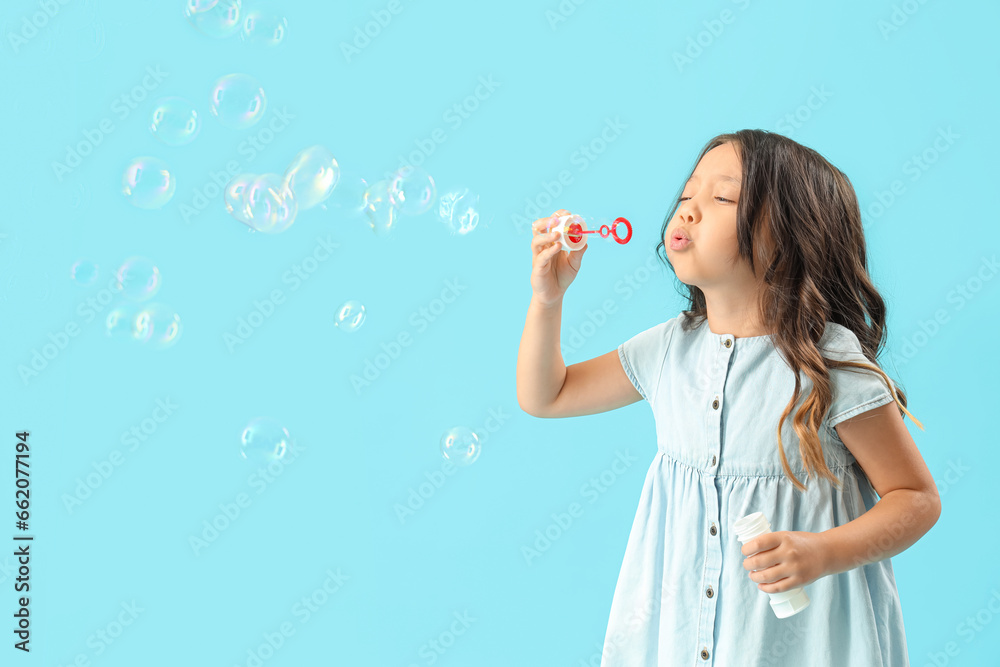 Cute little girl blowing soap bubbles on light blue background