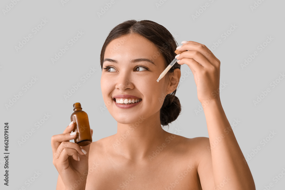 Beautiful Asian woman applying serum on light background, closeup