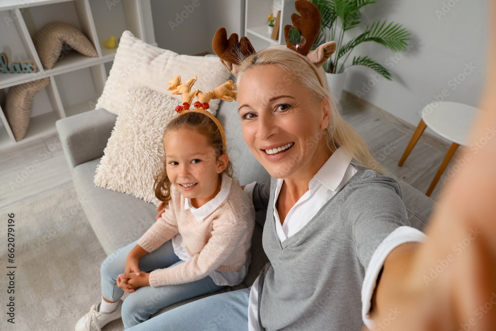 Little girl with her grandmother in reindeer horns taking selfie at home on Christmas eve