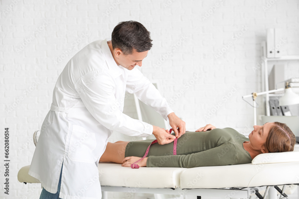 Male doctor measuring belly of pregnant woman in clinic