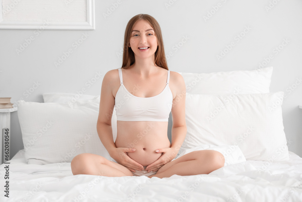 Young pregnant woman sitting in bedroom