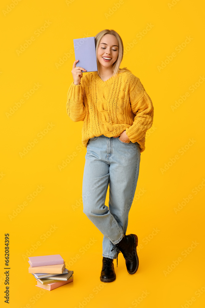 Beautiful young happy woman with many books on yellow background