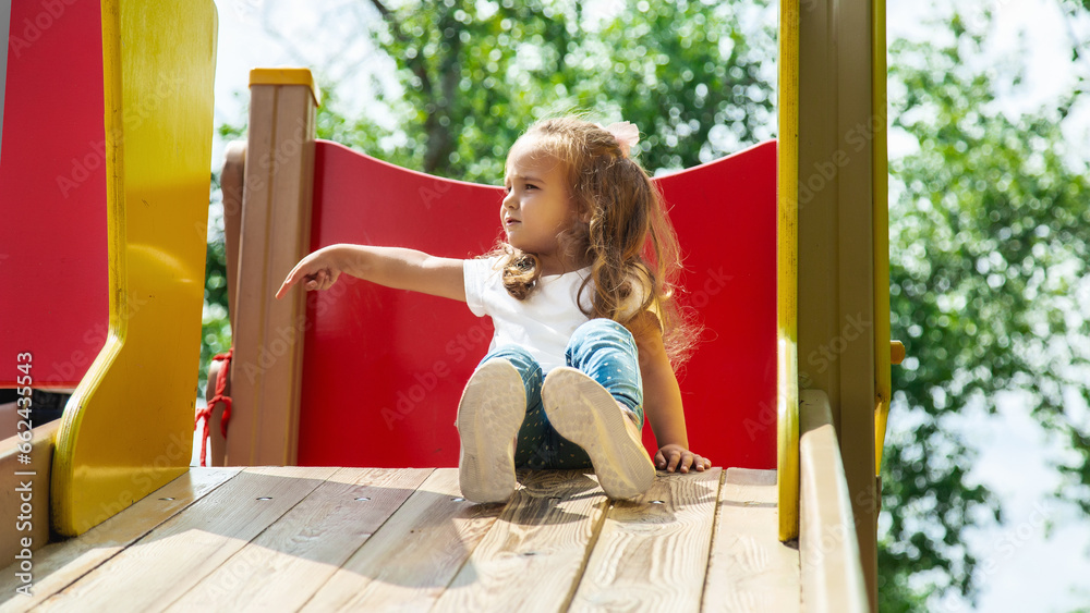 Child playing on outdoor playground. Kids play on school or kindergarten yard. Active kid on colorful slide and swing. Little girl on outdoors.