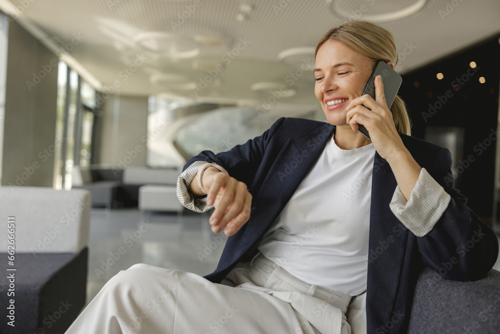 Female sales manager looking at wristwatch to checking time while having a phone call with client