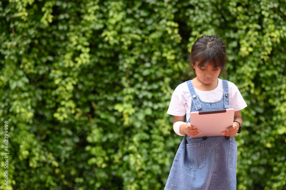 Cute girl in casual clothes listening to music and learning on your digital tablet in the park.