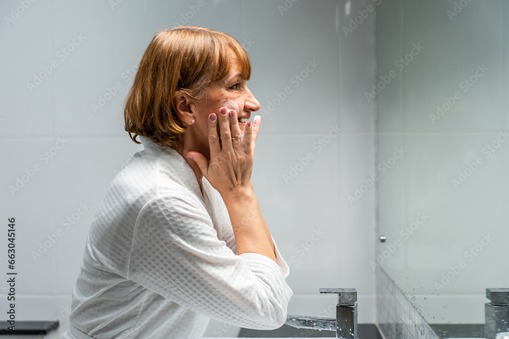 Caucasian senior woman wash and clean face with facial foam and water. 