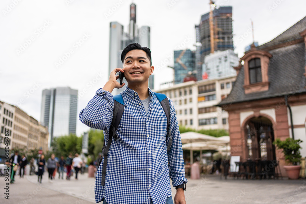 Asian young man backpacker talking on the phone while walking in city. 