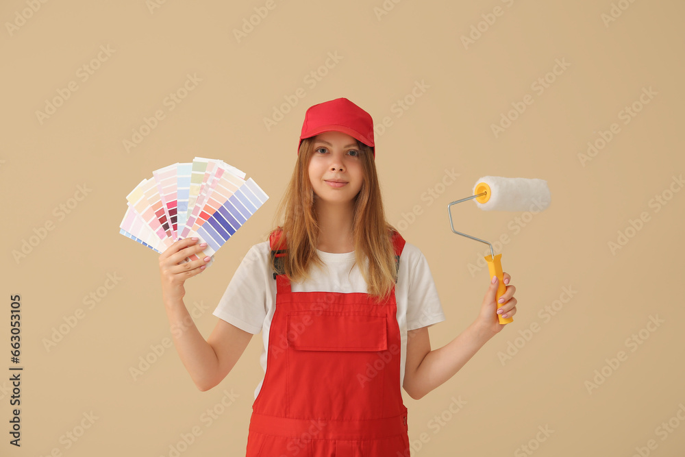 Female decorator with color samples and paint roller on beige background