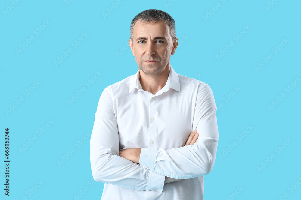 Portrait of handsome mature man with crossed arms on blue background