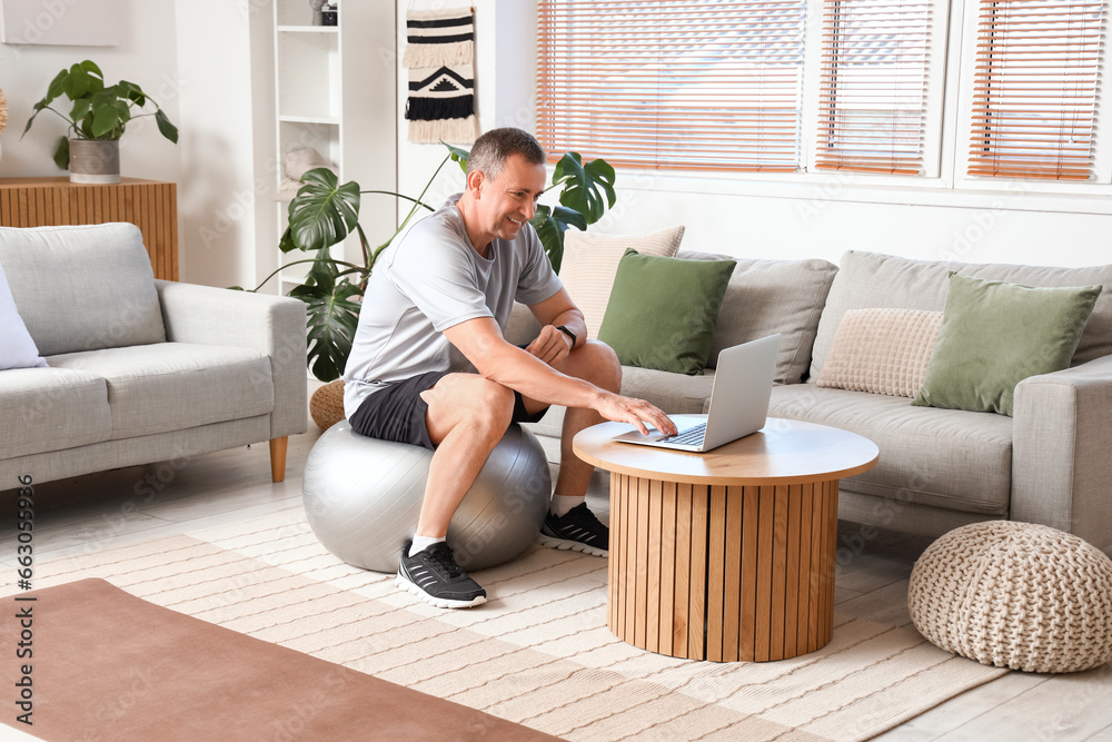 Sporty mature man with laptop on fitball at home