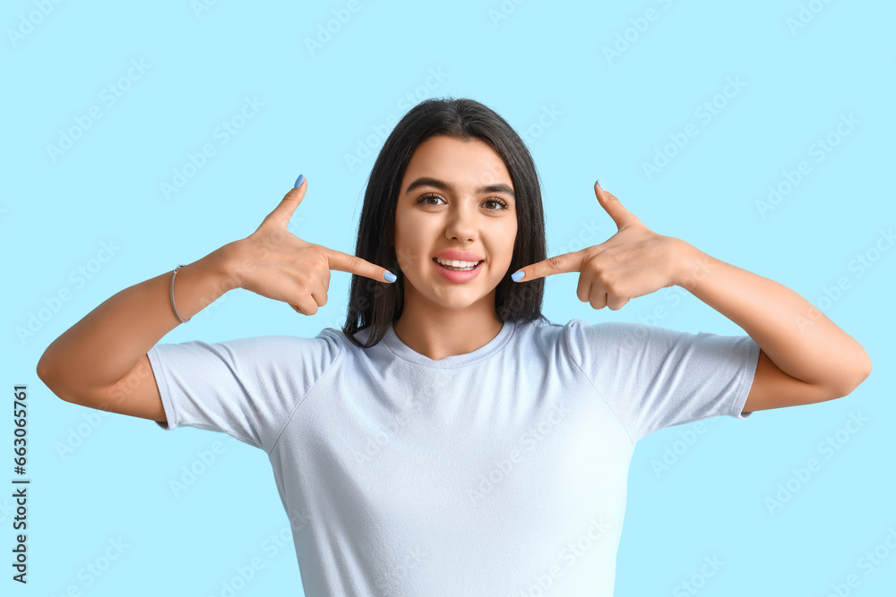 Young woman pointing at her smile on blue background