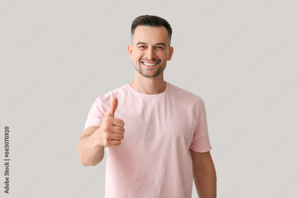 Happy young man showing thumb-up on light background