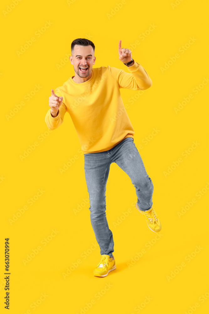 Happy young man pointing at something on yellow background