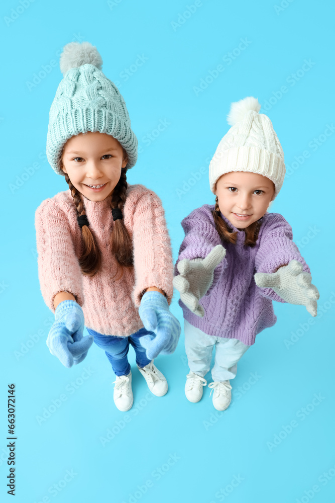 Cute little girls in warm clothes on blue background