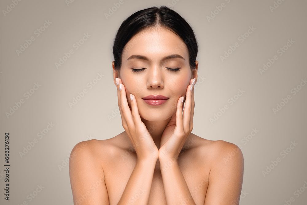 Calm positive pretty young european woman with perfect skin and closed eyes, touching hands to face