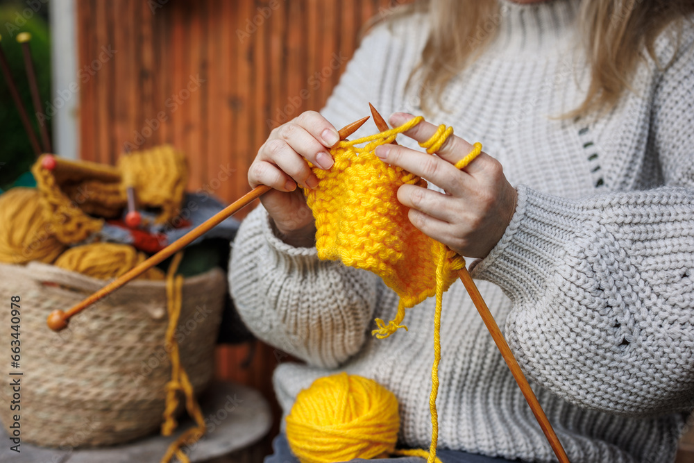 Knitting with wool. Woman in woolen sweater knits warm clothing of yellow yarn