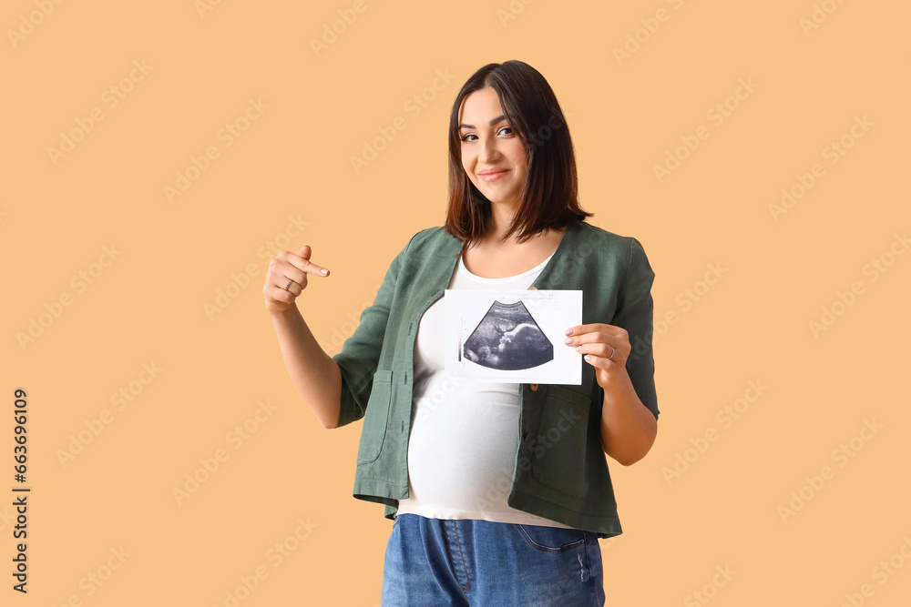 Young pregnant woman pointing at sonogram image on beige background