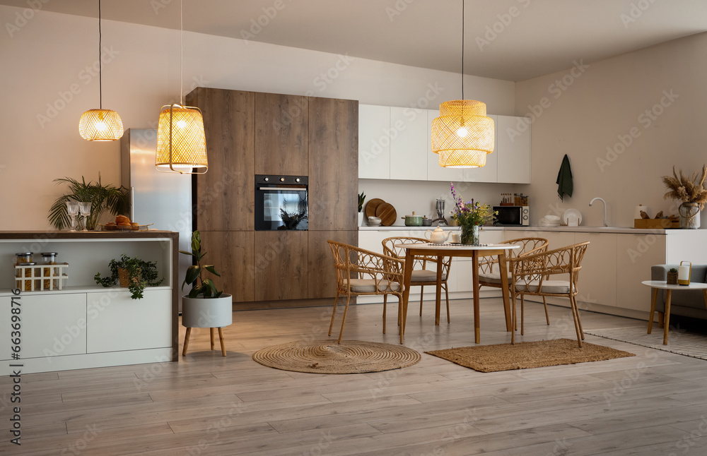 Interior of modern kitchen with dining table, island and glowing lamps