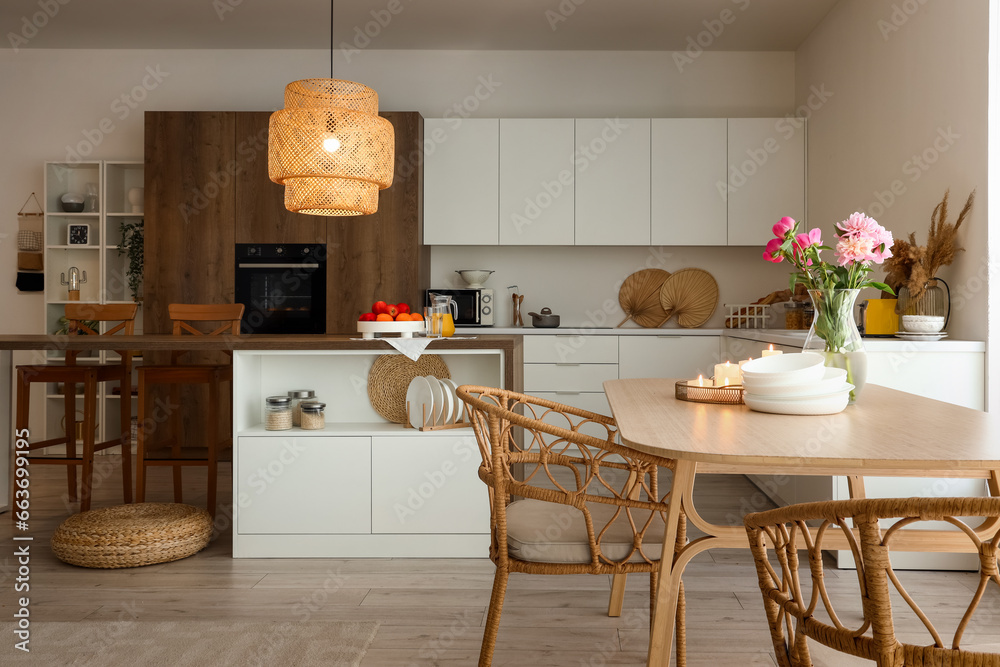 Dining table with peony flowers, burning candles and bowls in modern kitchen with glowing lamp