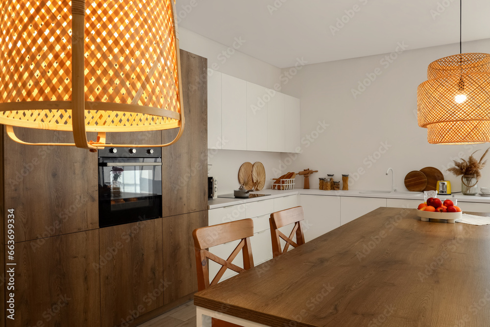 Interior of modern kitchen with wooden island table and glowing lamps