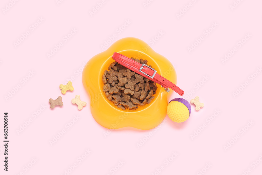 Bowl of dry pet food, collar and toy ball on pink background