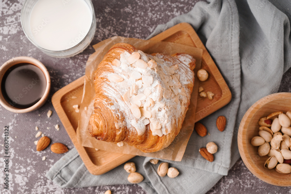 Wooden board of sweet croissant with powdered sugar and nuts on dark table