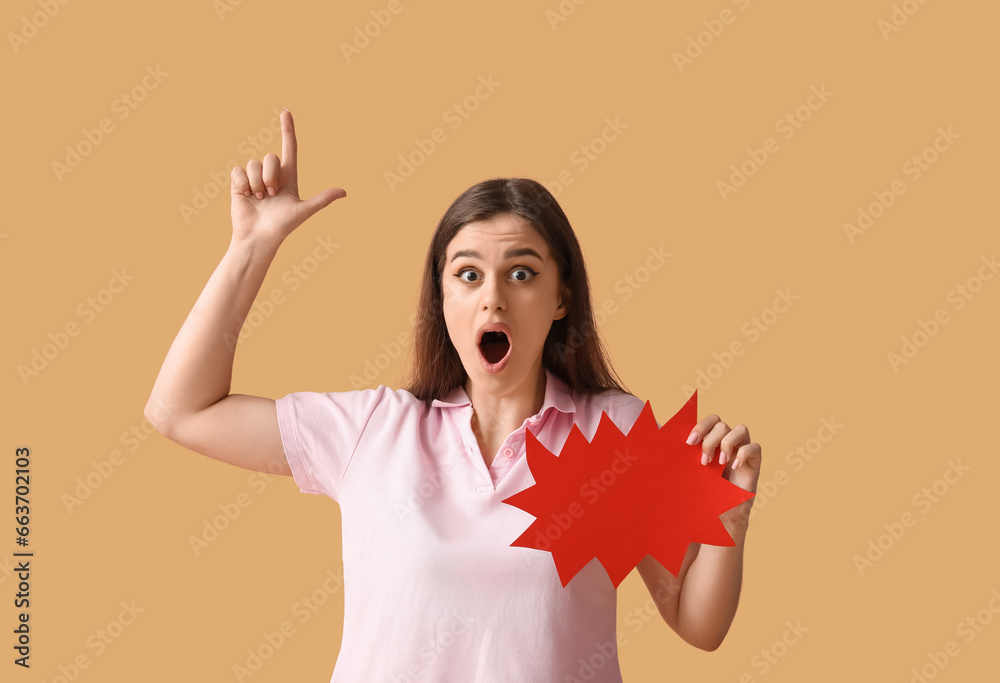 Beautiful shocked young woman with speech bubble pointing at something on orange background