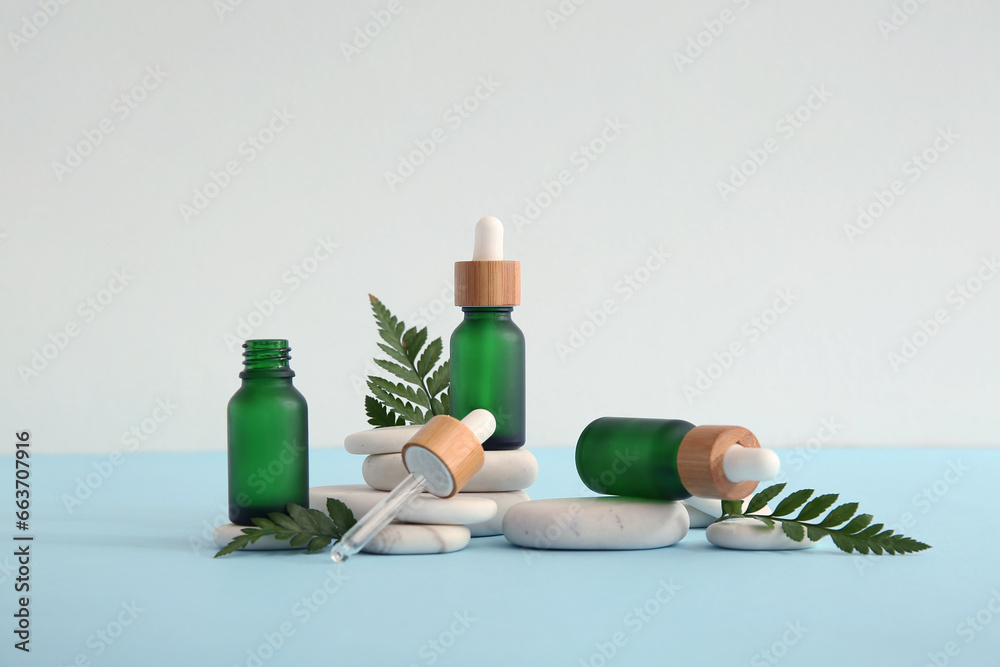 Composition with bottles of essential oil, stones and green leaves on light background