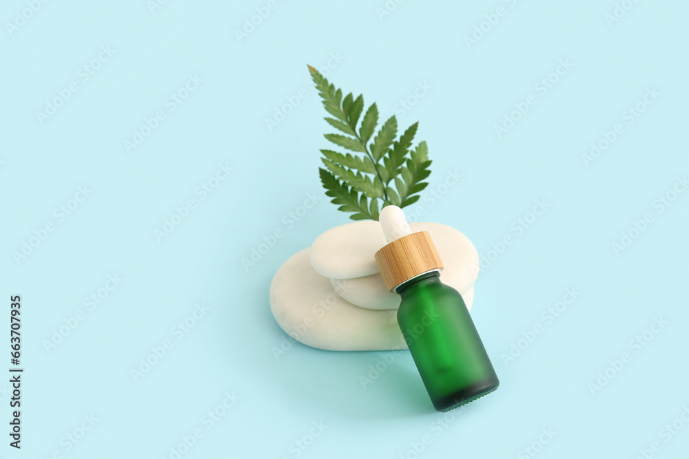 Composition with bottle of essential oil, green leaf and stones on blue background