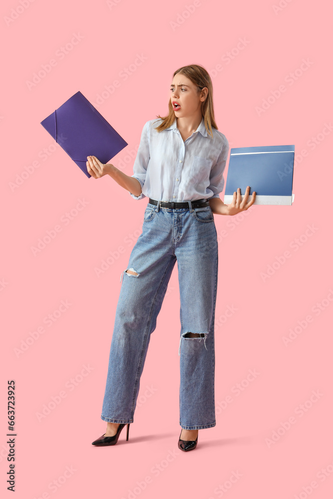 Stressed young businesswoman with document folders on pink background