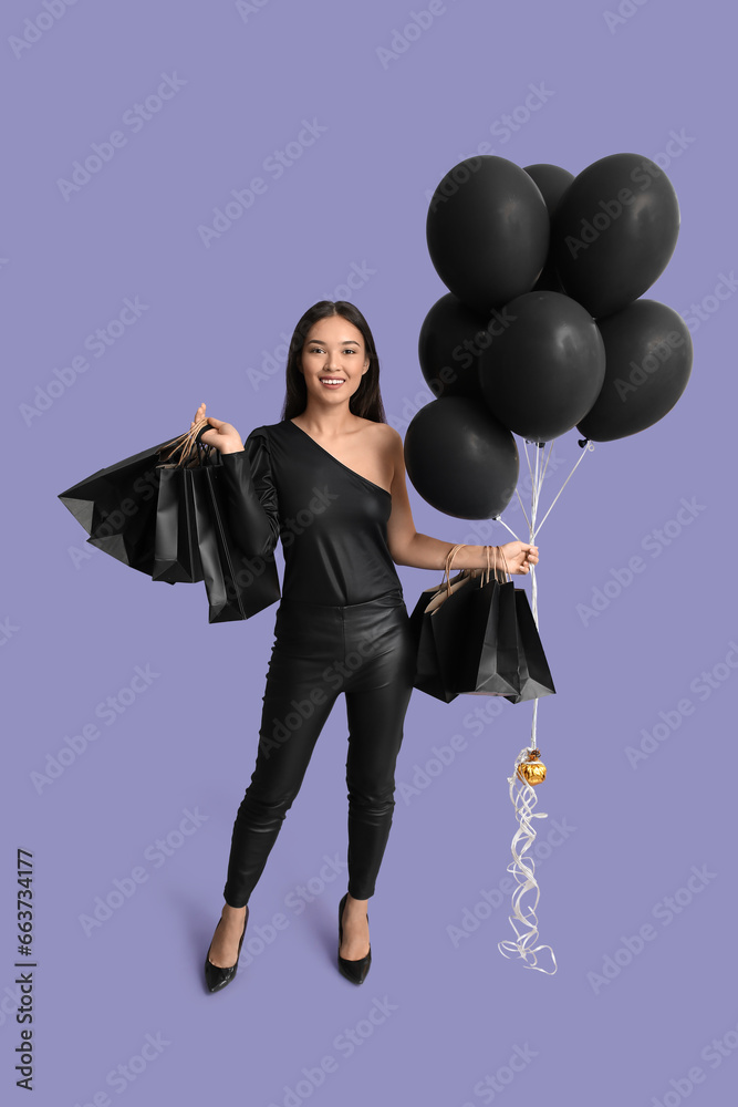 Beautiful young Asian woman with shopping bags and balloons on purple background. Black Friday sale