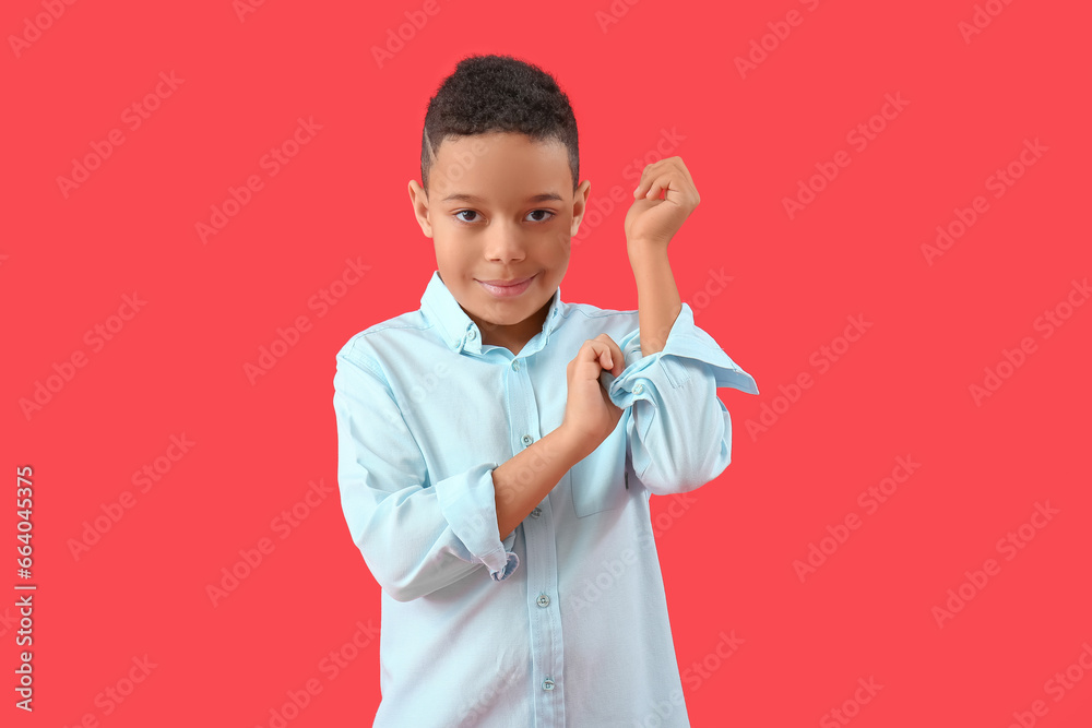 Little African-American boy rolling up his sleeve on red background