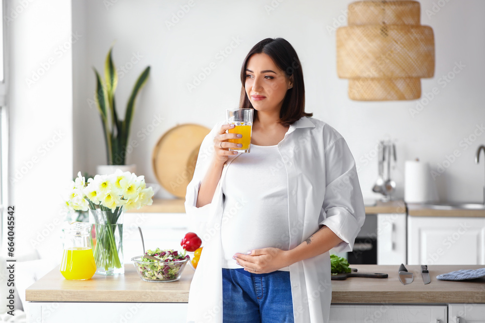 Young pregnant woman with glass of juice in kitchen