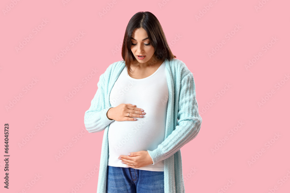 Shocked young pregnant woman on pink background