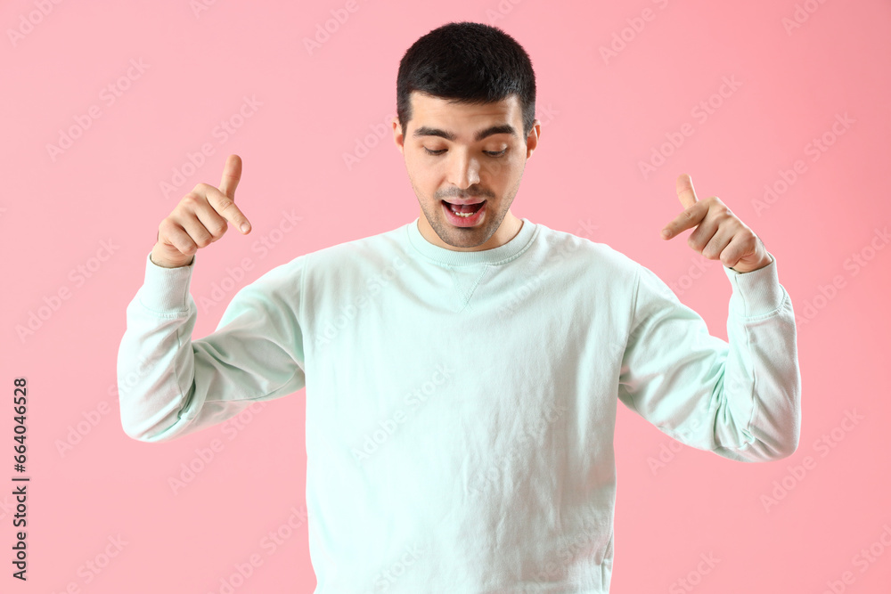 Young man pointing at something on pink background