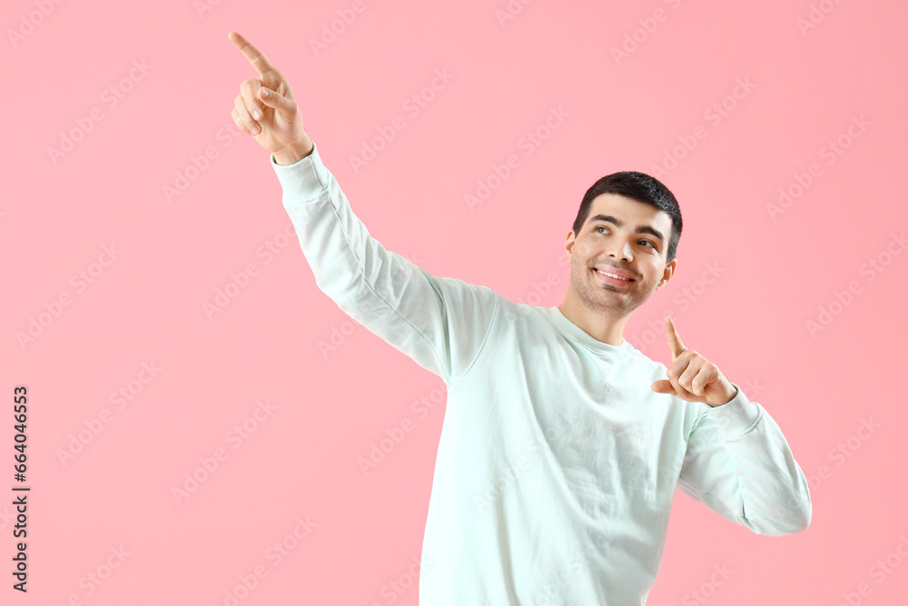 Young man pointing at something on pink background