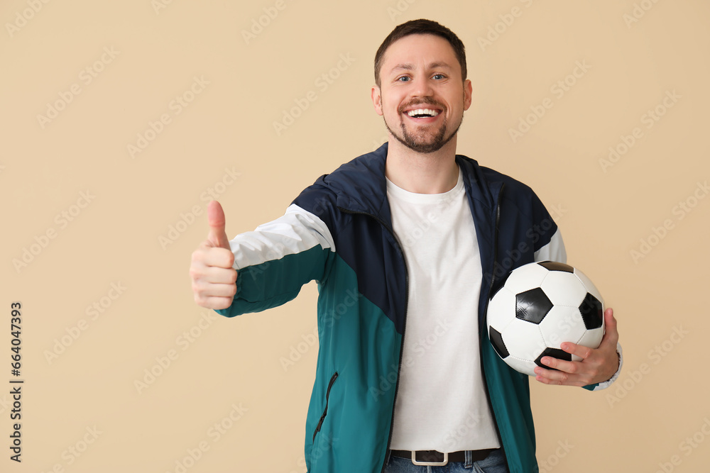 Happy man with soccer ball showing thumb-up on beige background