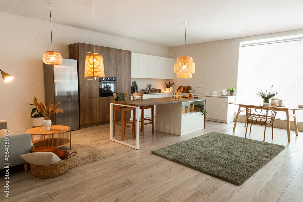 Interior of modern open plan kitchen with island table and glowing lamps